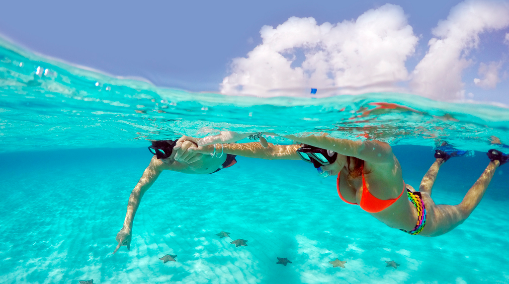 Pareja realiza Snorkel, agua transparente en el fondo estrellas de mar